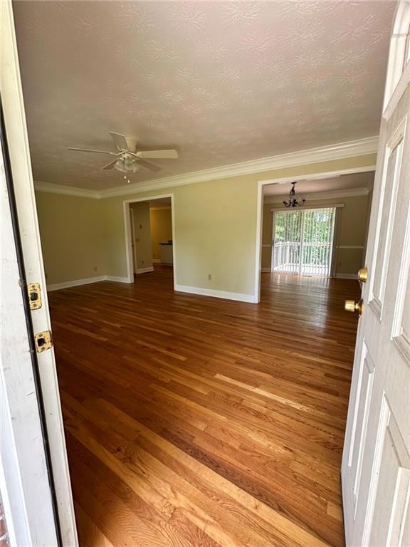 Empty room featuring a chandelier, wood finished floors, baseboards, ceiling fan, and ornamental molding