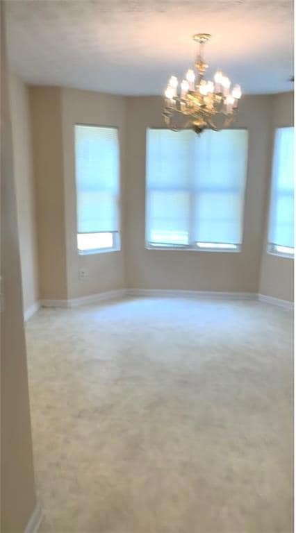 Unfurnished room featuring a chandelier and baseboards