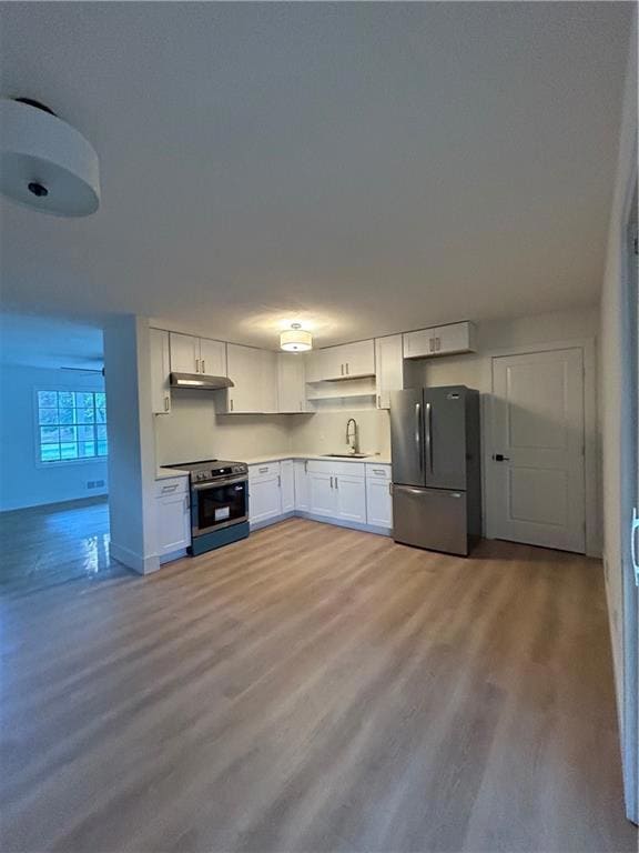 Kitchen featuring white cabinets, refrigerator, range, and light wood-style flooring