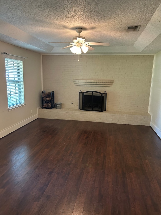 Unfurnished living room with a textured ceiling, wood finished floors, brick wall, a fireplace, and a ceiling fan