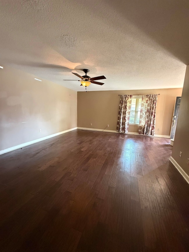 Empty room featuring a textured ceiling, dark wood-type flooring, and ceiling fan
