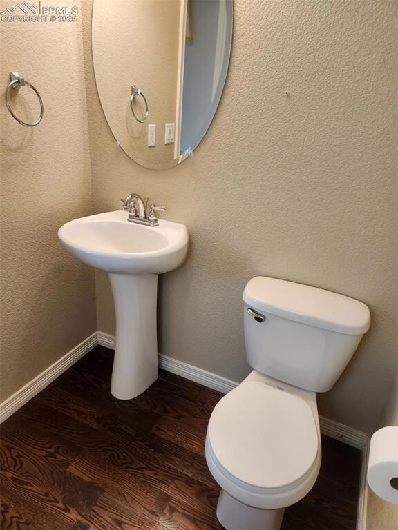 Half bathroom featuring wood finished floors, toilet, baseboards, and a sink