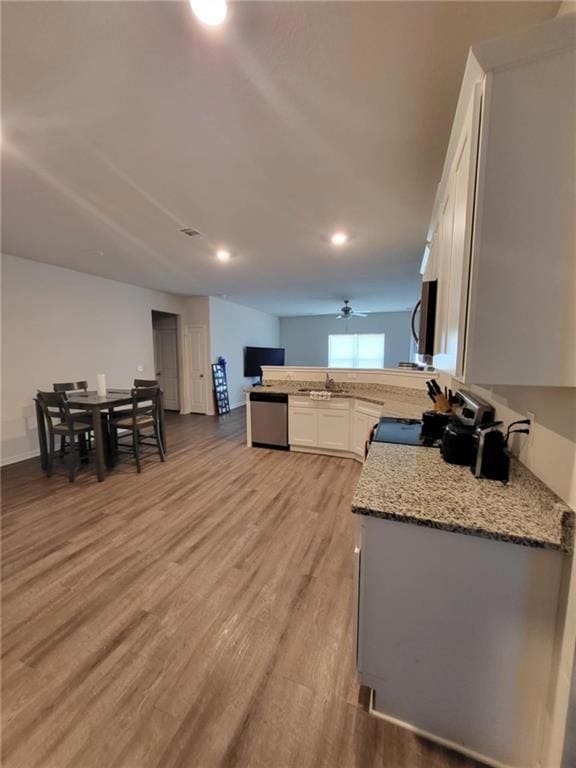 Kitchen with stainless steel appliances, white cabinetry, light stone countertops, light wood-style flooring, and ceiling fan