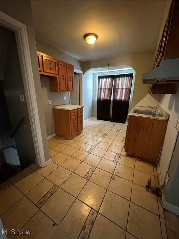 Kitchen featuring brown cabinetry, arched walkways, extractor fan, light countertops, and light tile patterned floors