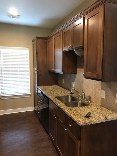 Kitchen featuring light stone countertops, backsplash, dark wood finished floors, black dishwasher, and dark brown cabinetry