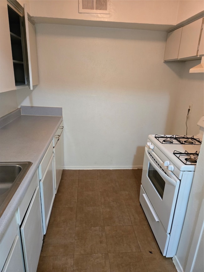 Kitchen featuring range, white cabinetry, light countertops, and dark tile patterned flooring