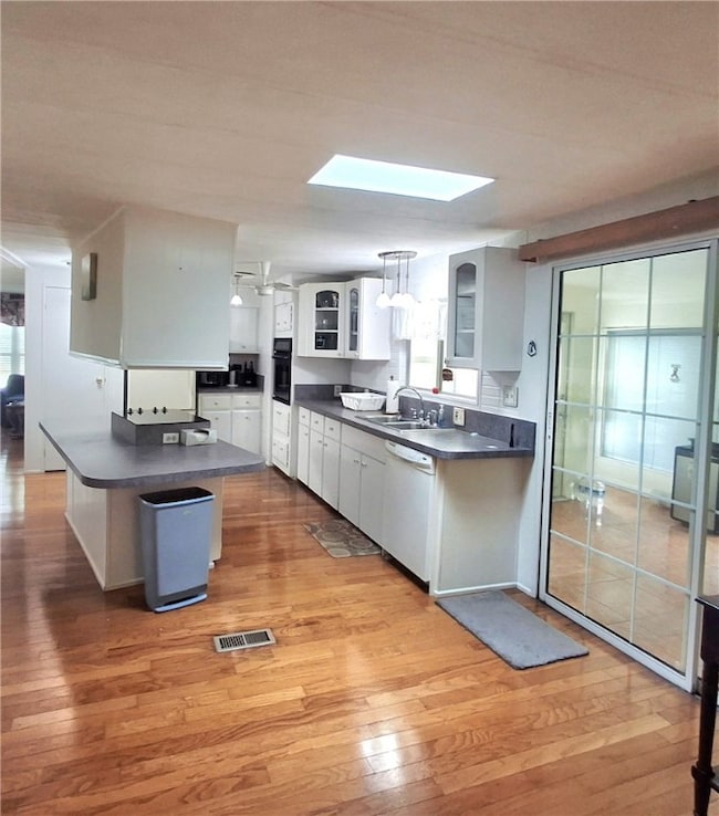 Kitchen featuring dark countertops, white cabinets, light wood finished floors, and glass insert cabinets