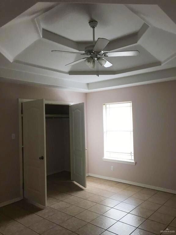Unfurnished bedroom featuring coffered ceiling, light tile patterned flooring, a closet, ceiling fan, and beamed ceiling