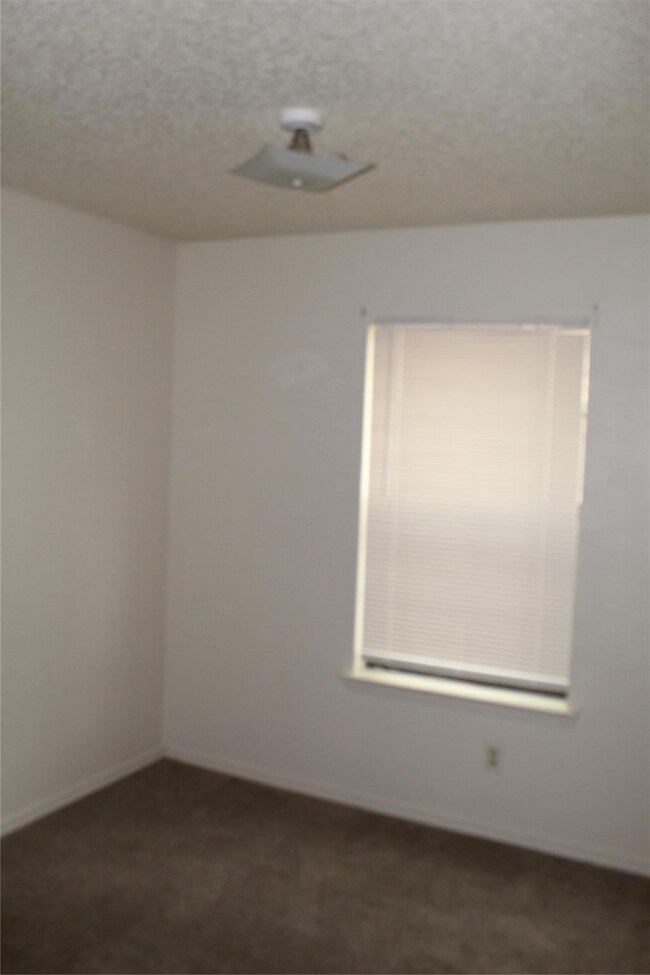 Empty room featuring dark carpet and a textured ce