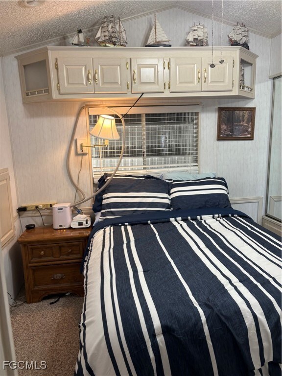 Bedroom featuring wood walls, carpet floors, Built in closets, lofted ceiling, and a textured ceiling