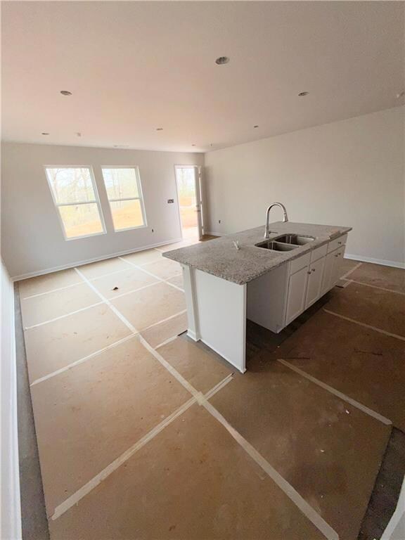 Kitchen featuring a kitchen island with sink, a sink, open floor plan, white cabinets, and light stone countertops