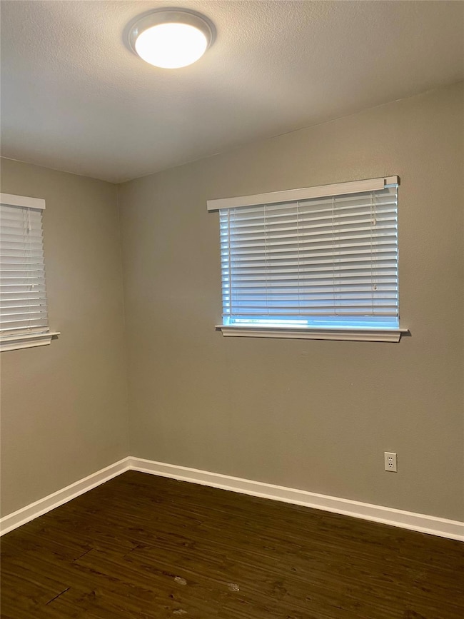 Unfurnished room with dark wood-type flooring, healthy amount of natural light, and a textured ceiling