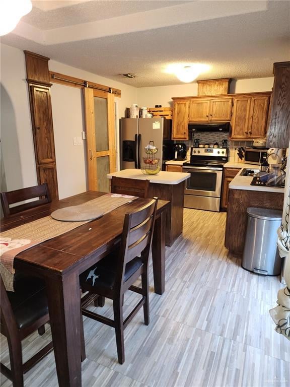 Kitchen featuring appliances with stainless steel finishes, backsplash, a textured ceiling, a kitchen island, and a barn door