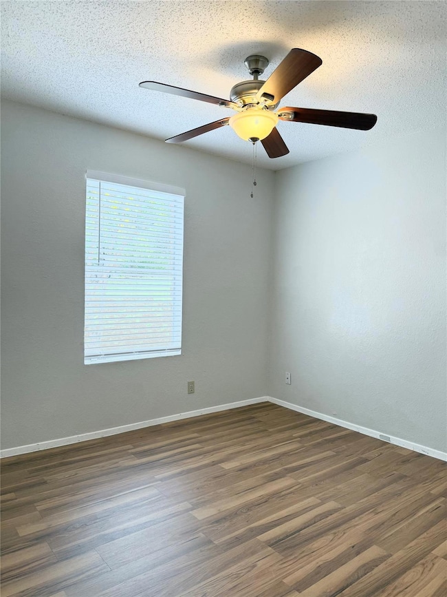 Empty room with a textured ceiling, dark wood-type flooring, and a ceiling fan