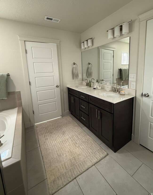 Bathroom with double vanity, light tile patterned flooring, a textured ceiling, and tiled tub