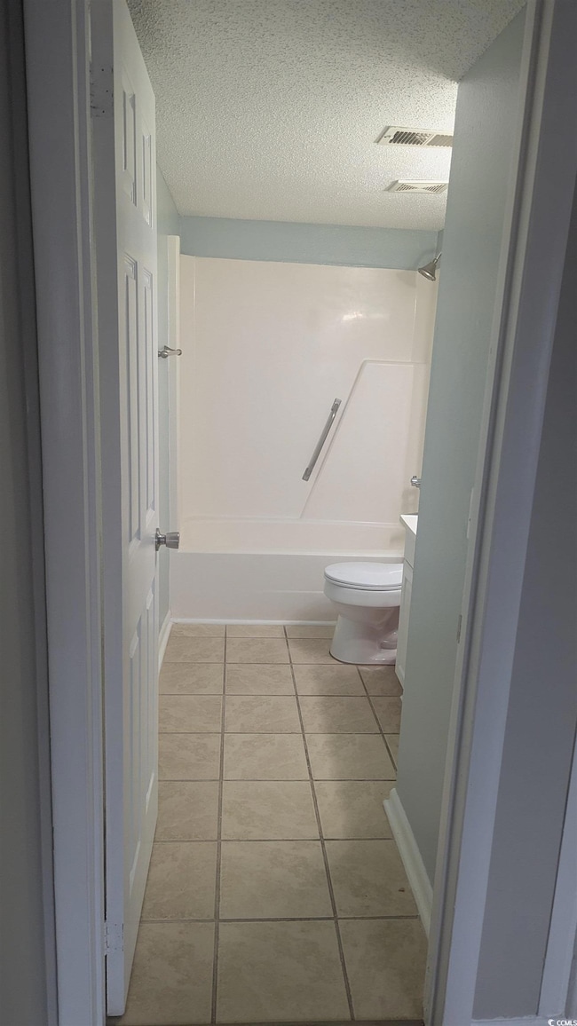 Bathroom with toilet, a textured ceiling, tile patterned flooring, vanity, and tub / shower combination