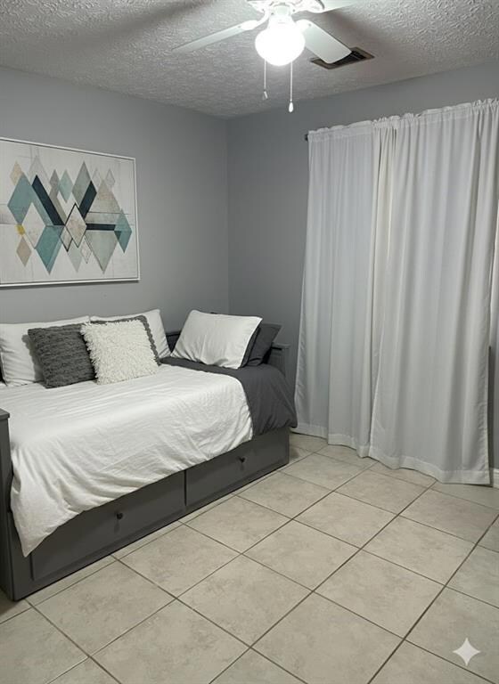 Bedroom featuring a textured ceiling, light tile patterned floors, and a ceiling fan.  Staged Photo.