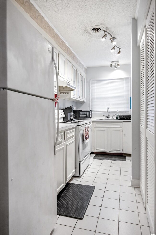 Kitchen with freestanding refrigerator, white electric range, under cabinet range hood, a sink, and a textured ceiling