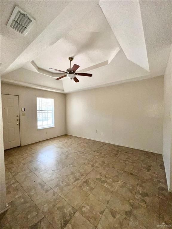 Living room with a tray ceiling, a ceiling fan, visible vents, and a textured ceiling