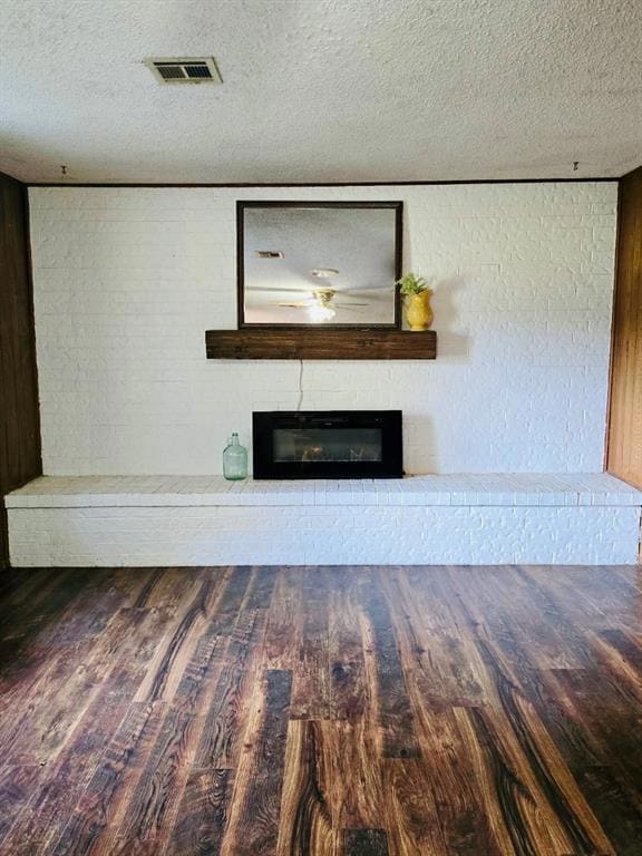 Unfurnished living room with a textured ceiling, wood finished floors, and a brick fireplace