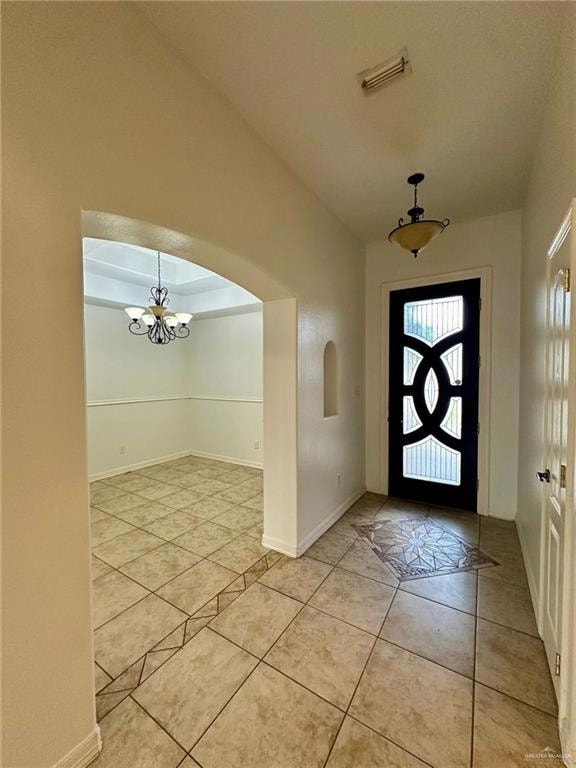 Foyer with light tile patterned floors, arched walkways, a chandelier, baseboards, and lofted ceiling