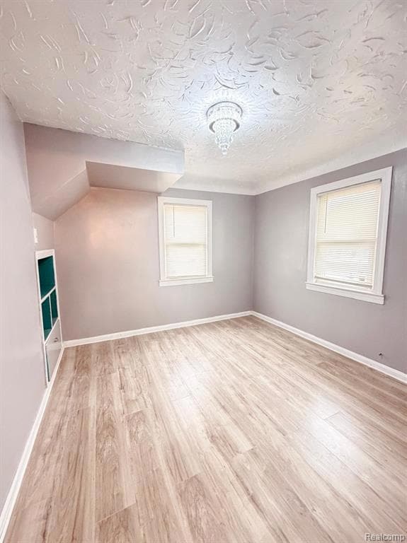 Additional living space with light wood-style flooring and a textured ceiling