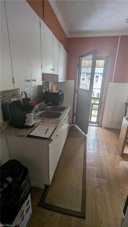 Kitchen featuring sink, white cabinets, ornamental molding, backsplash, and light hardwood floors