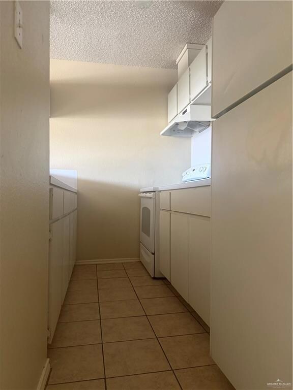 Kitchen featuring stove, white cabinetry, exhaust hood, light tile patterned flooring, and a textured ceiling