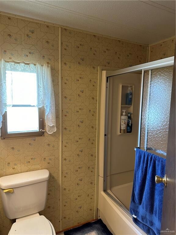 Bathroom featuring shower / bath combination with glass door, toilet, and a textured ceiling