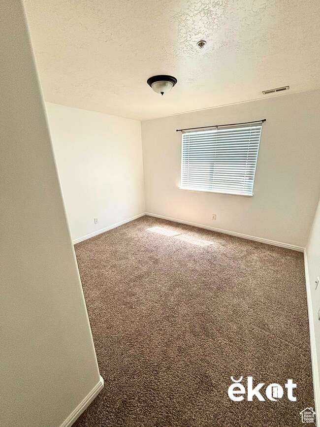 Carpeted spare room with a textured ceiling and baseboards