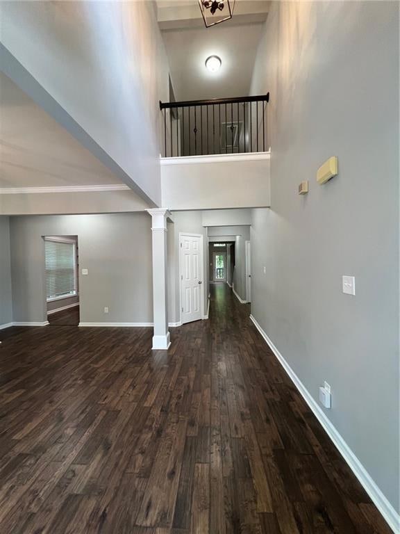Unfurnished living room featuring wood finished floors, a high ceiling, baseboards, and decorative columns