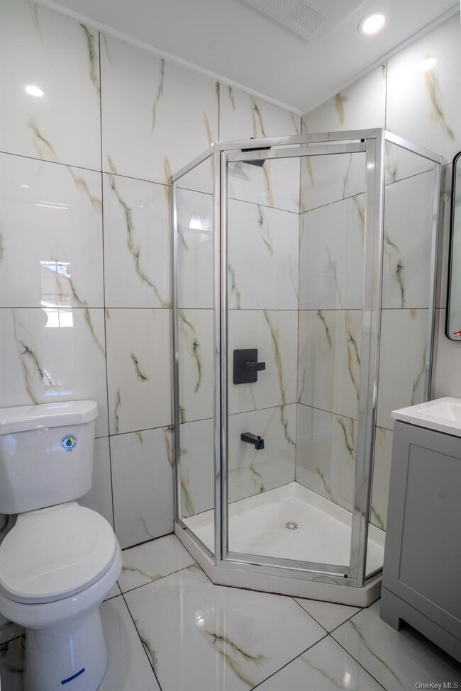 Bathroom featuring a marble finish shower, vanity, tile walls, and recessed lighting