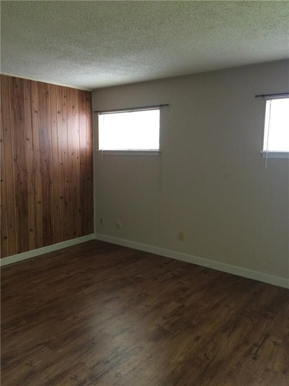 Empty room featuring wood walls, a textured ceiling, and dark wood-style floors