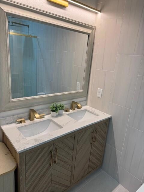 Full bath with double vanity, a sink, and tile wal