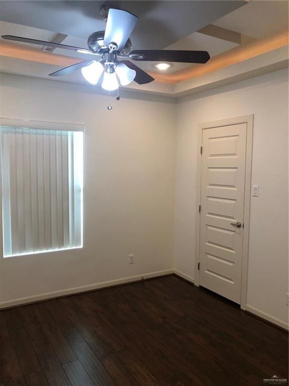 Unfurnished room featuring baseboards, ceiling fan, a tray ceiling, and dark wood-style floors