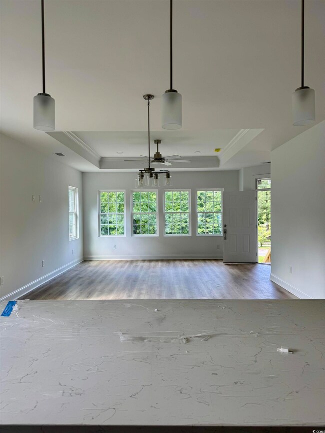 Unfurnished living room featuring a raised ceiling, wood finished floors, a ceiling fan, and ornamental molding
