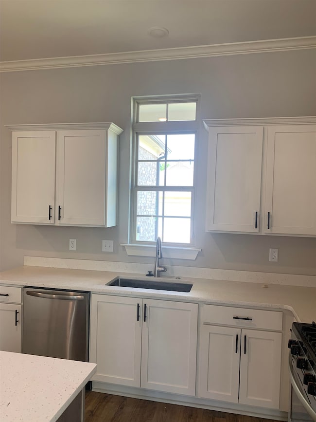 Kitchen featuring stainless steel appliances, white cabinetry, solid surface countertops, and crown molding Window over sink