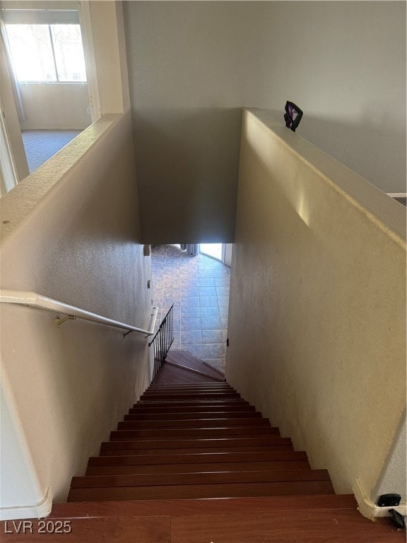 Stairs featuring healthy amount of natural light, wood finished floors, and a textured wall