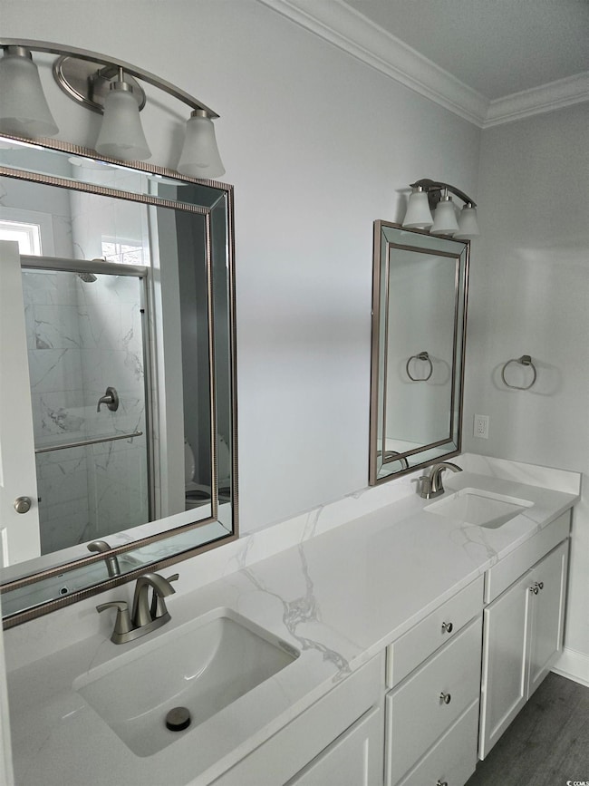Bathroom with a marble finish shower, ornamental molding, double vanity, and a sink
