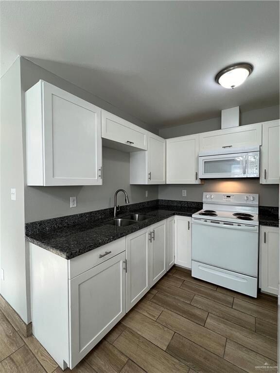Kitchen with stove, dark wood-style floors, white cabinetry, and dark stone counters