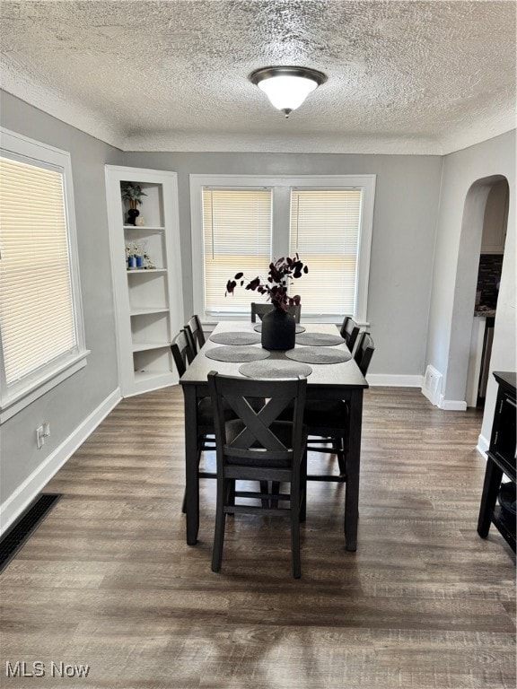 Dining space featuring arched walkways, dark wood-style flooring, a textured ceiling, and built in features