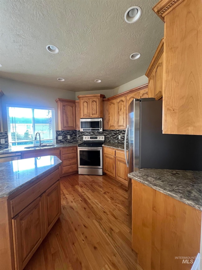 Kitchen with dark stone counters, stainless steel appliances, decorative backsplash, wood flooring, and a textured ceiling