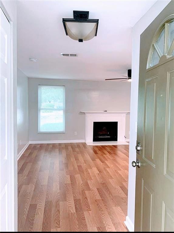 Unfurnished living room featuring light wood-style floors, a ceiling fan, and a fireplace