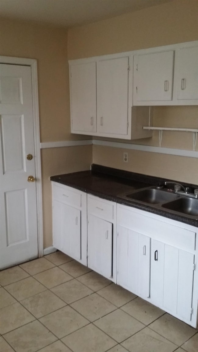 Kitchen with white cabinets, light tile patterned floors, and dark countertops