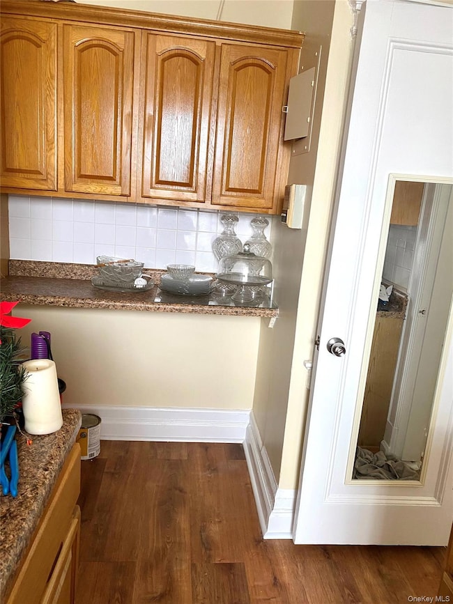 Kitchen with tasteful backsplash, brown cabinetry, and dark wood-style flooring