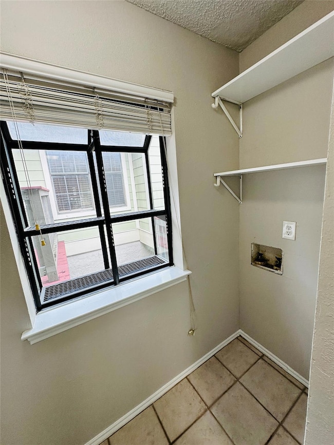 Laundry room featuring a textured ceiling, light tile patterned flooring, and washer hookup