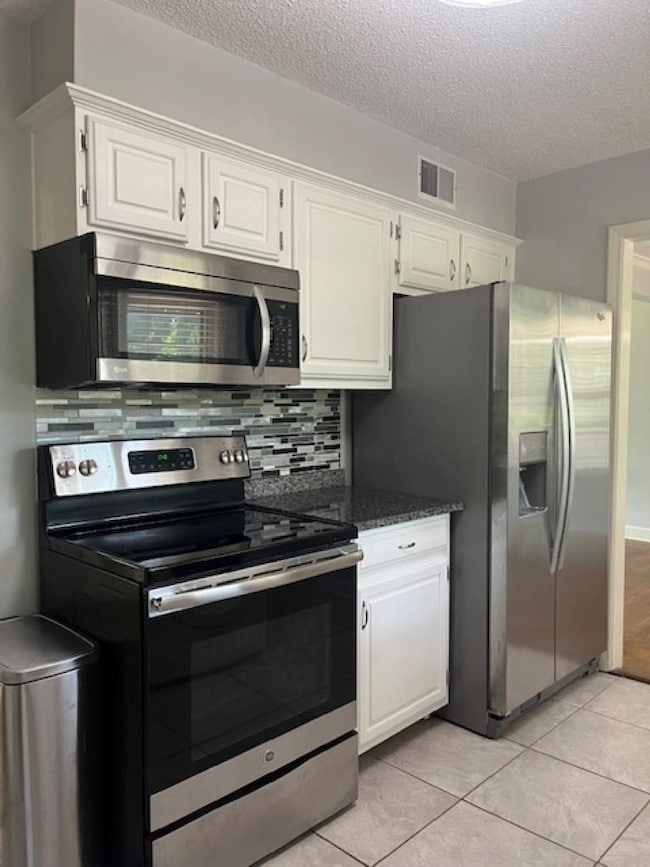 Kitchen with stainless steel appliances, white cabinets, a textured ceiling, and backsplash