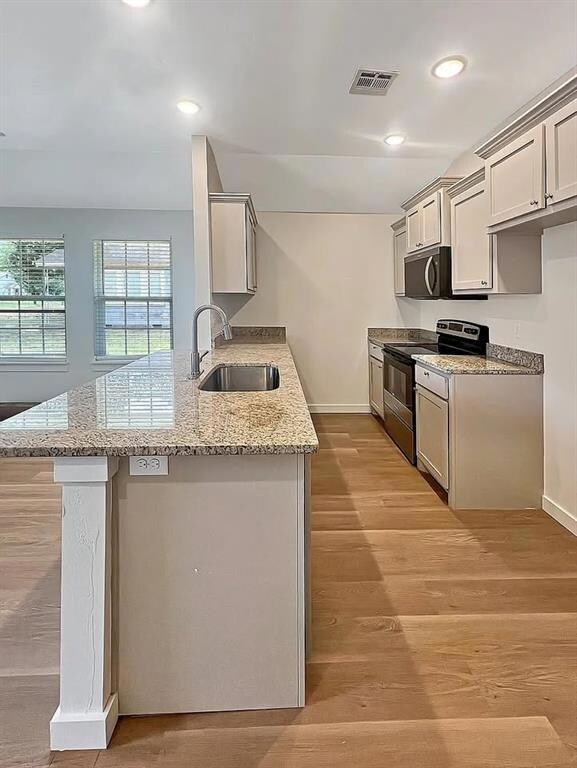 Kitchen featuring light wood-type flooring, open floor plan, light stone counters, healthy amount of natural light, and lofted ceiling.Note: Photos are of a similar home by the builder.