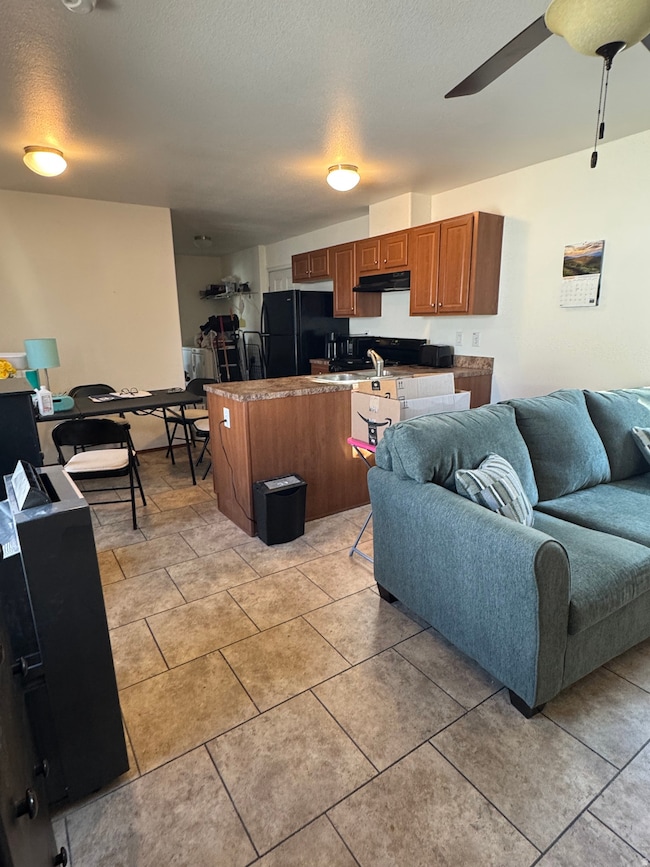 Living area with a textured ceiling, ceiling fan, and light tile patterned floors