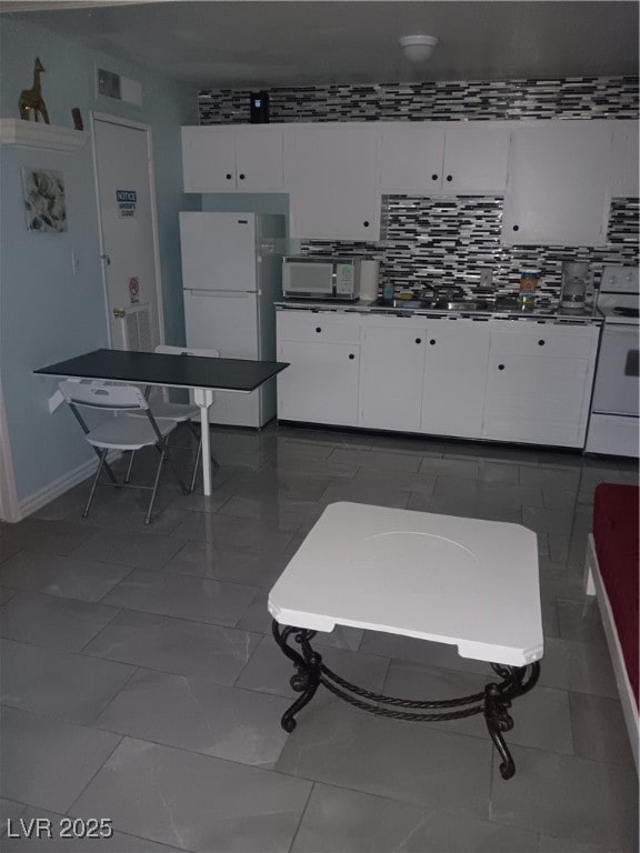 Kitchen featuring visible vents, range, fridge, baseboards, and white cabinets